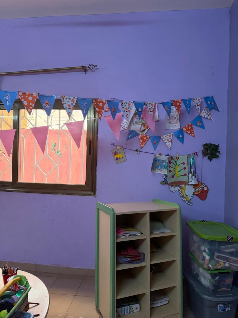 Espace repos aux murs violets avec fanions décoratifs, étagères et rideaux colorés — Complexe Rokia Traoré