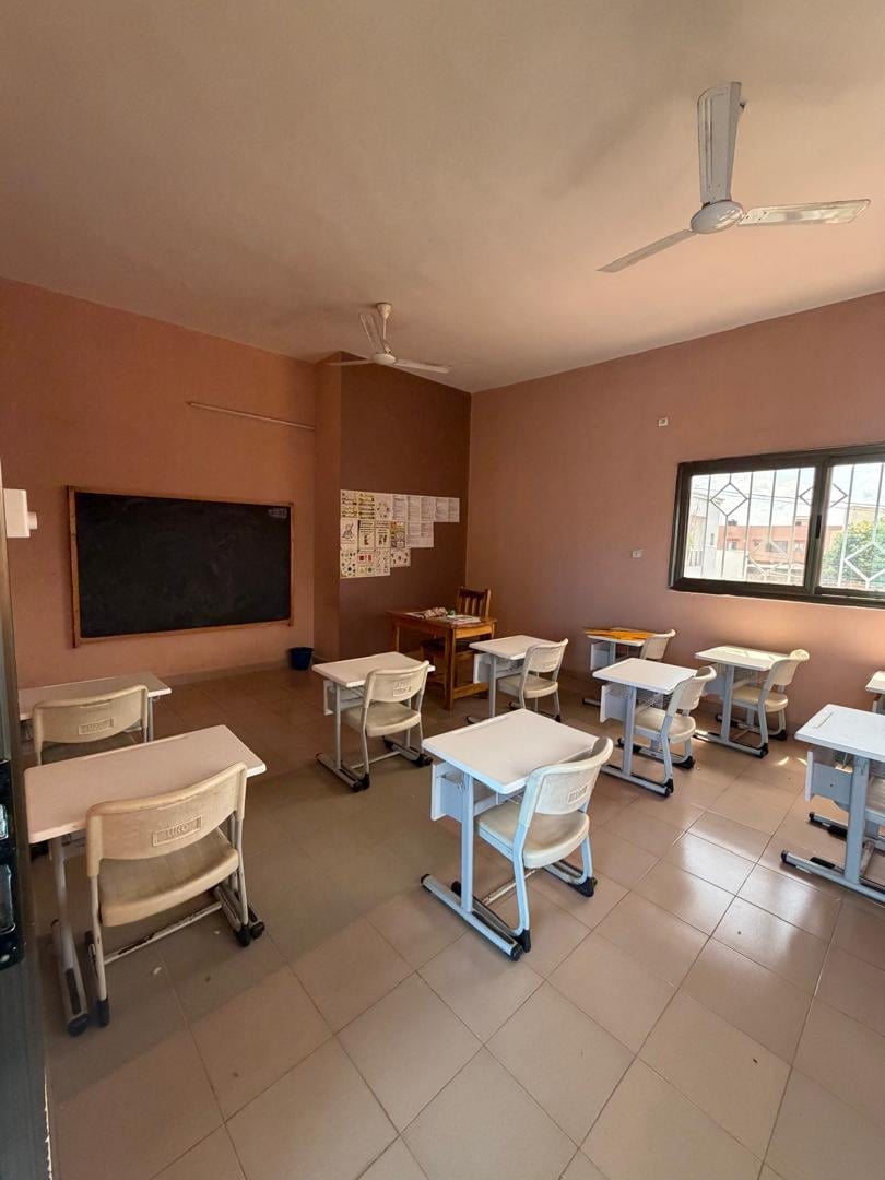 Salle de classe du primaire avec pupitres, tableau noir et grandes fenêtres — Complexe Rokia Traoré, Bamako