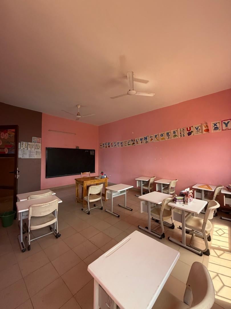 Salle rose avec affiches d'alphabet en cursive, pupitres individuels et tableau noir — section Grande Section du Complexe Rokia Traoré